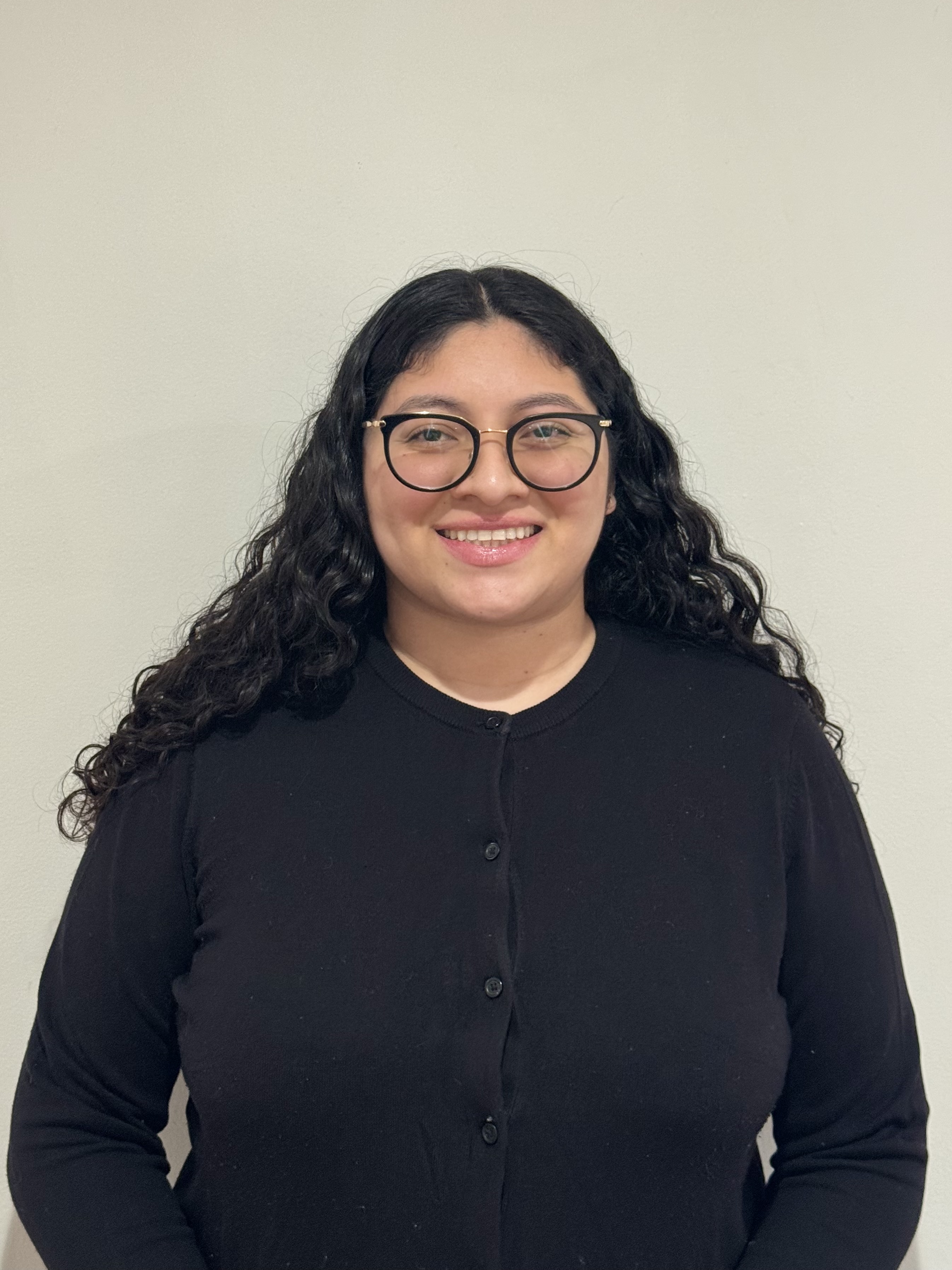 Cristy is a woman with round black glasses, a black button down sweater, and long dark, curly hair.