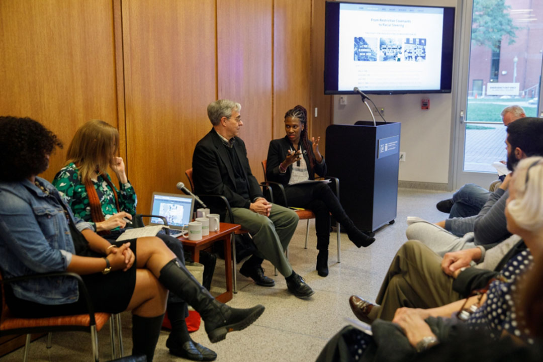 Gregory Squires speaks on a panel with a group of people at the front of a room