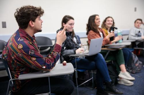 A student sitting at a desk speaks to three others in a classroom