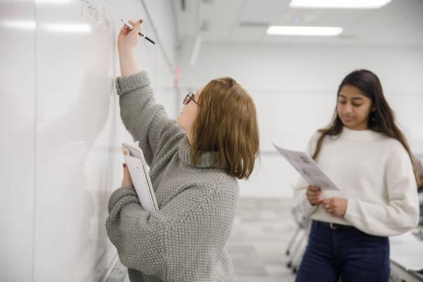 Two women talking and writing on a white board