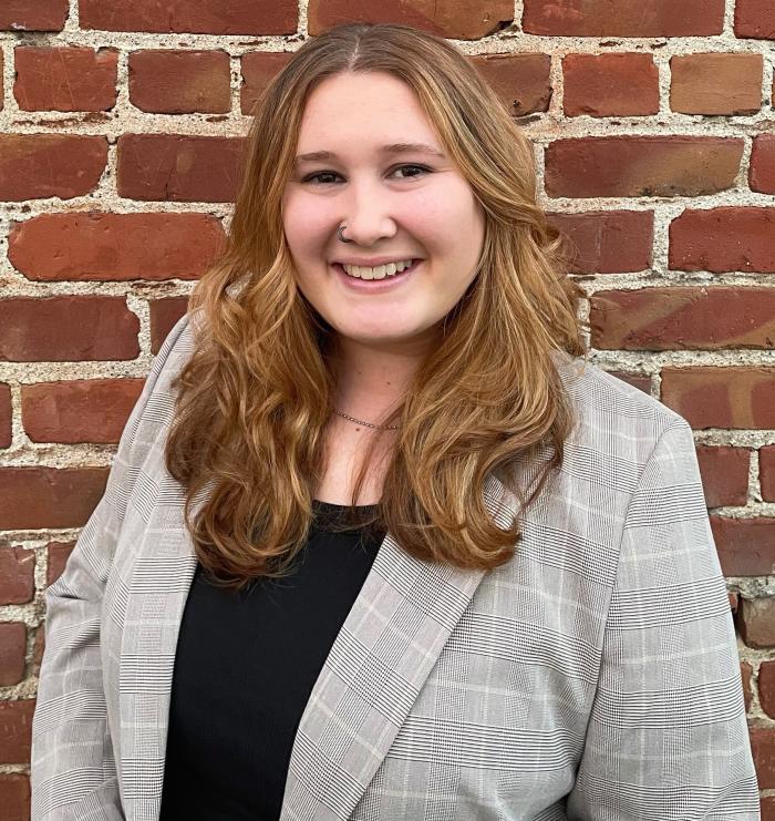 Kaitlyn DaVisio is a young white woman with brown-blonde hair. She is wearing a black shirt and a gray plaid jacket
