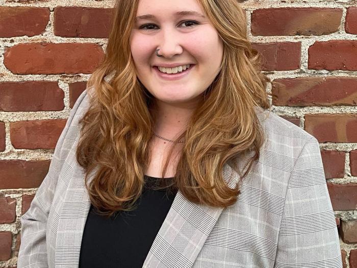 Kaitlyn DaVisio is a young white woman with brown-blonde hair. She is wearing a black shirt and a gray plaid jacket