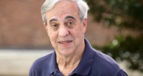 Gregory Squires is an older white man with white hair wearing a blue collared shirt 